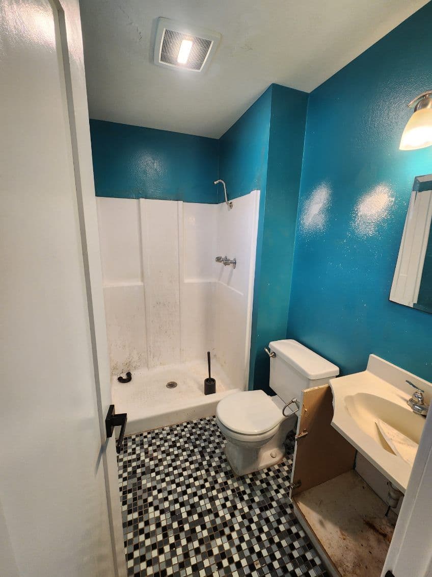 Bathroom with turquoise walls, black and white tiled floor, shower stall, and missing cabinet door.
