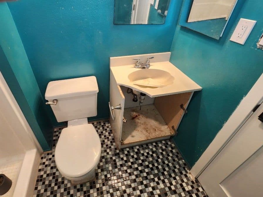 Bathroom with turquoise walls, a toilet, sink with missing cabinet door, and checkered tile floor.