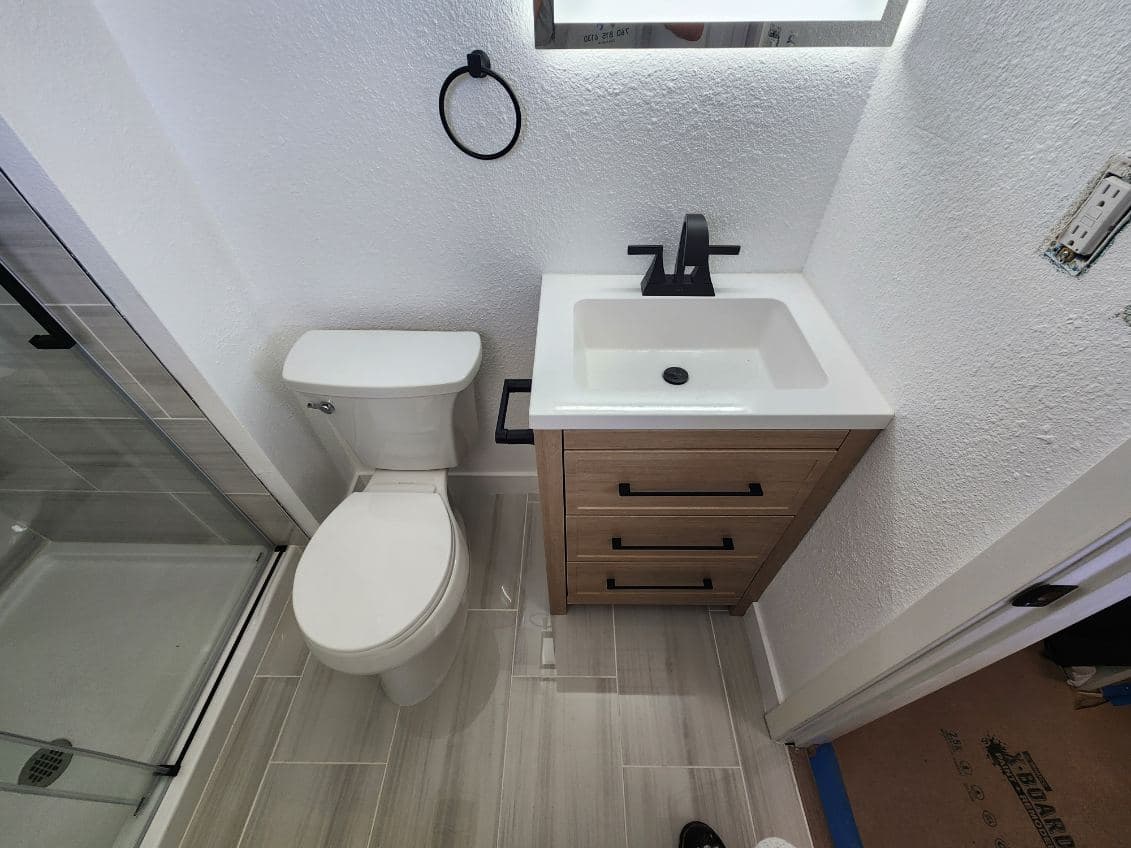 Modern bathroom design featuring a white toilet, sleek sink with black faucet, and wood storage cabinet.