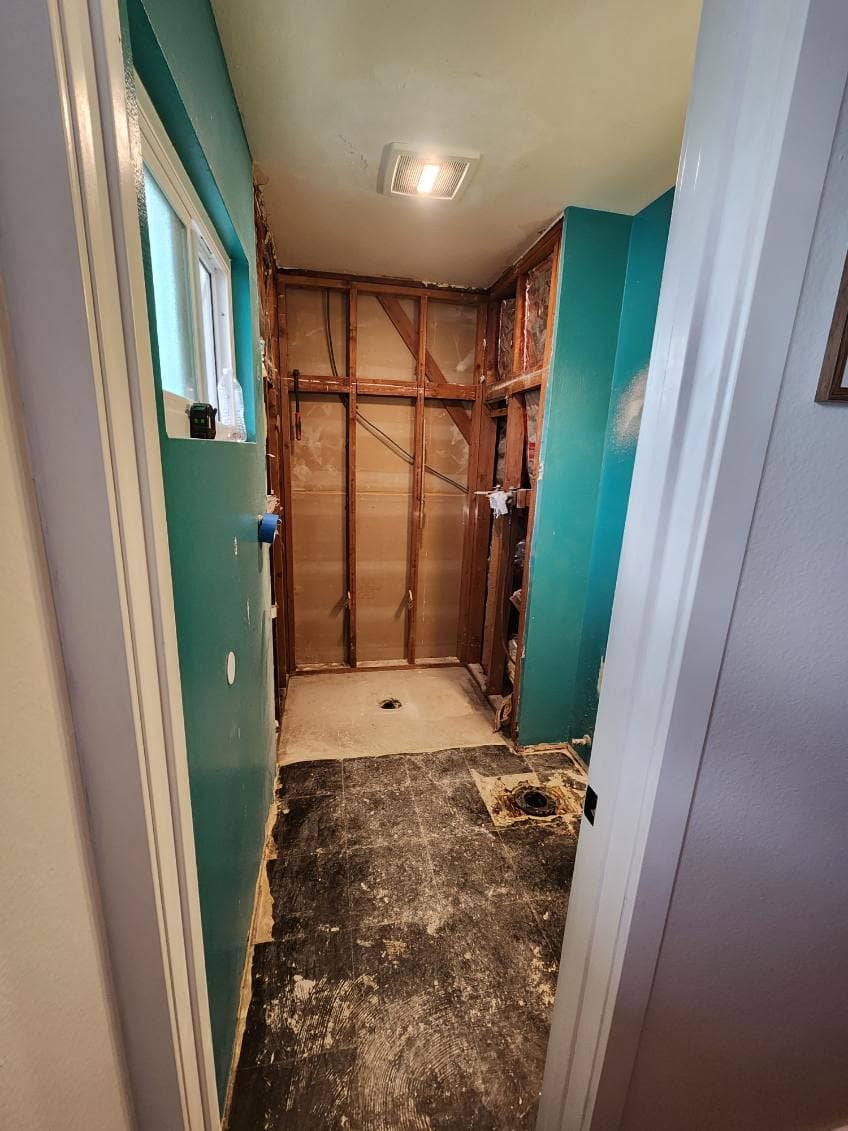Bathroom renovation in progress, showcasing exposed walls and flooring. Bright teal paint.