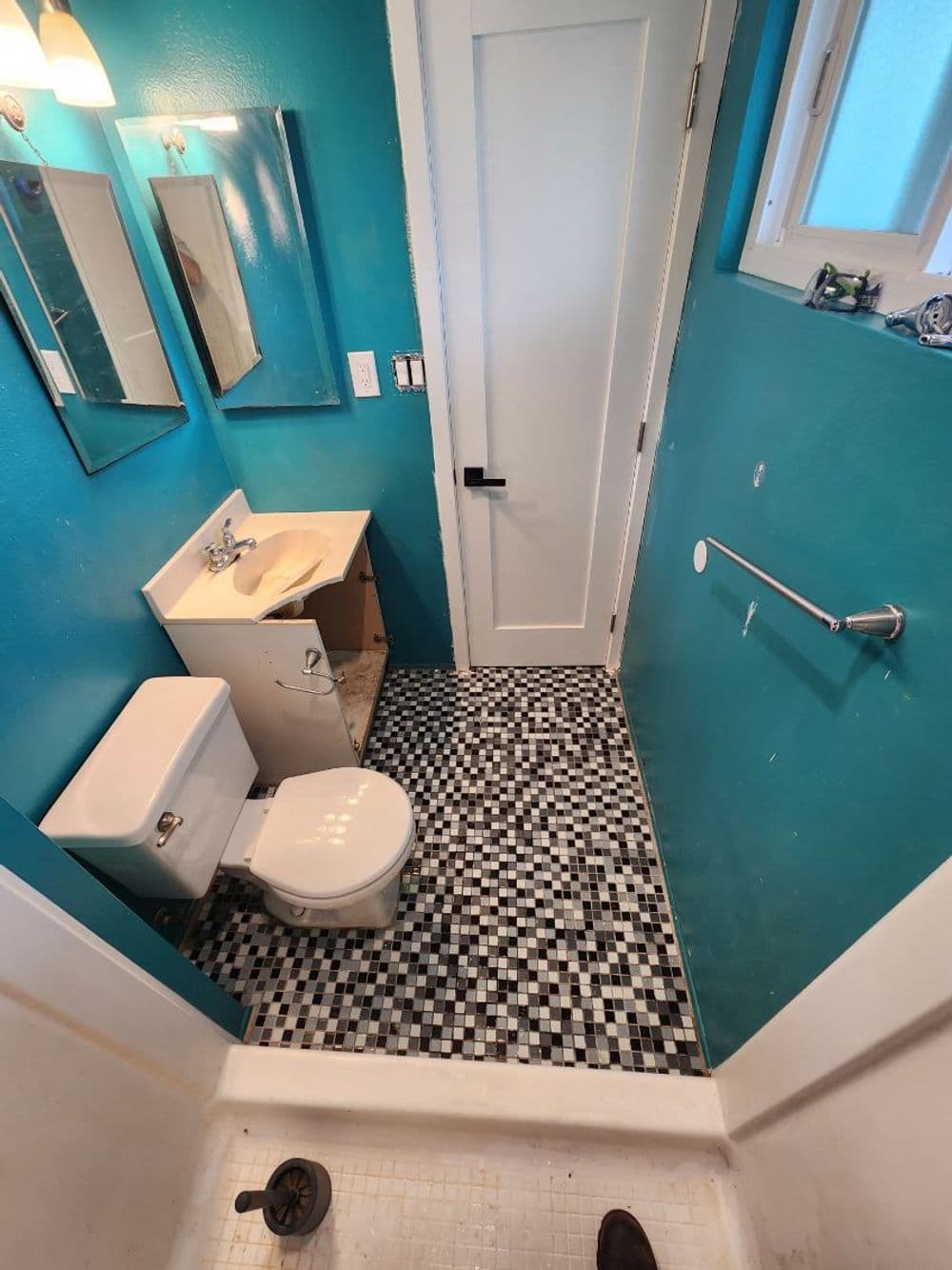 Small bathroom with turquoise walls, tiled floor, sink, toilet, and mirrors.